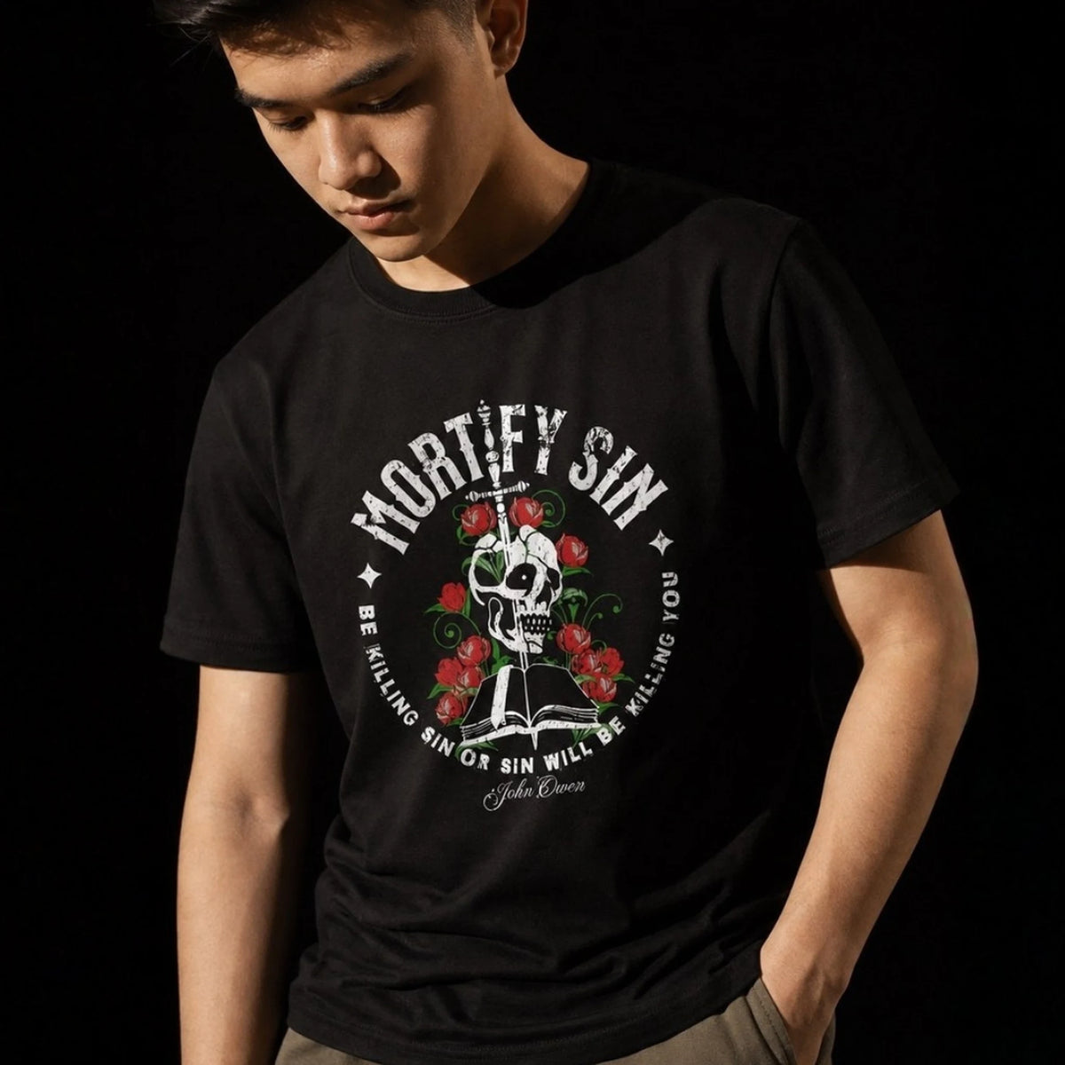 Close-up of Mortify Sin graphic on black unisex T-shirt worn by male model