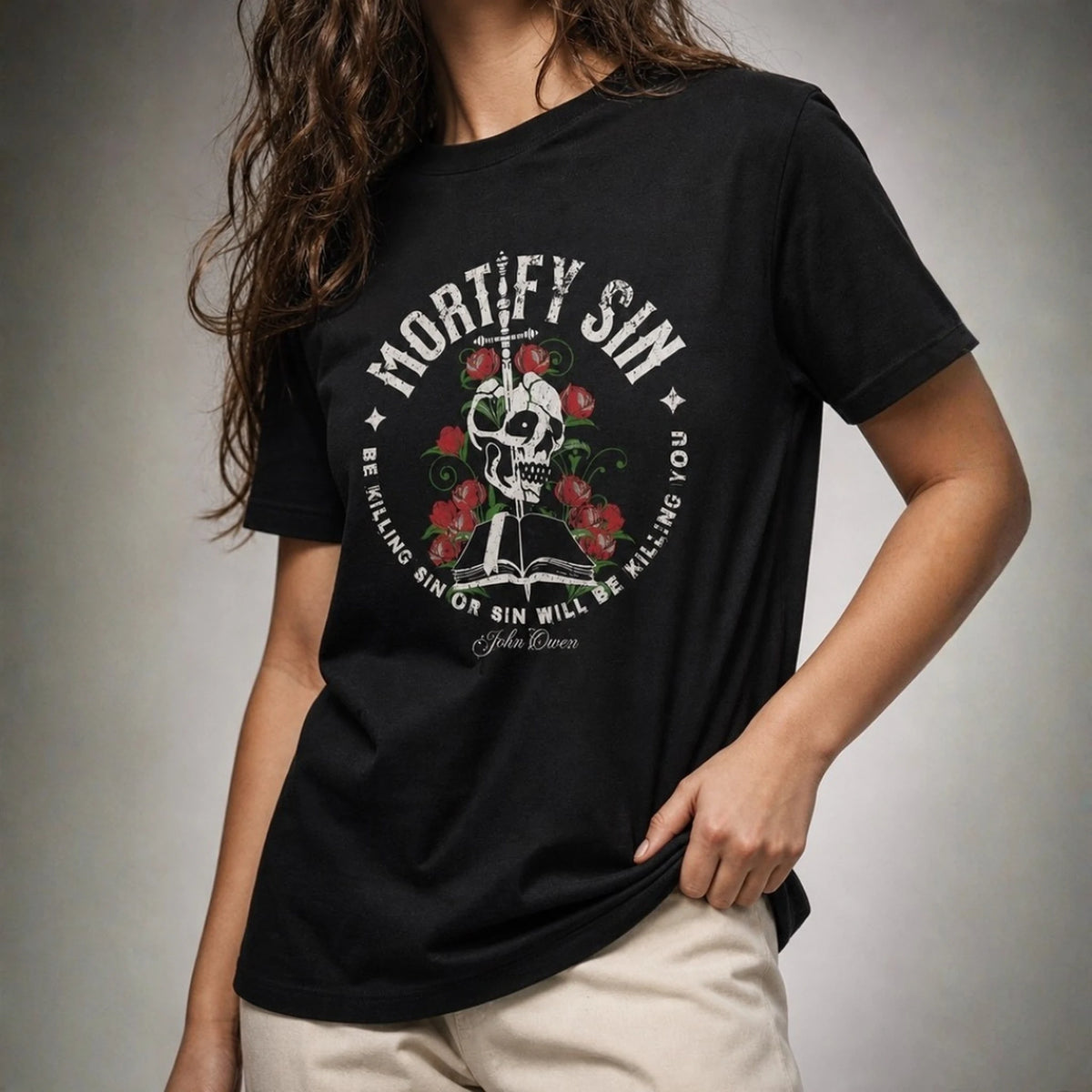 Close-up of Mortify Sin graphic on black unisex T-shirt worn by female model