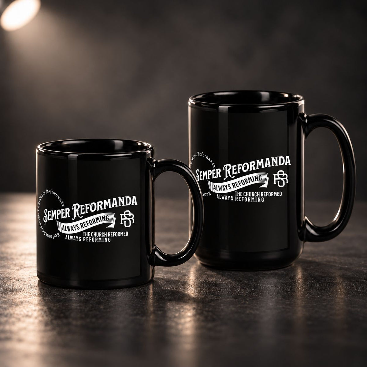 Two glossy black ceramic mugs with white 'Semper Reformanda' text and emblem printed on the side, displayed on a dark reflective surface against a moody dark background.